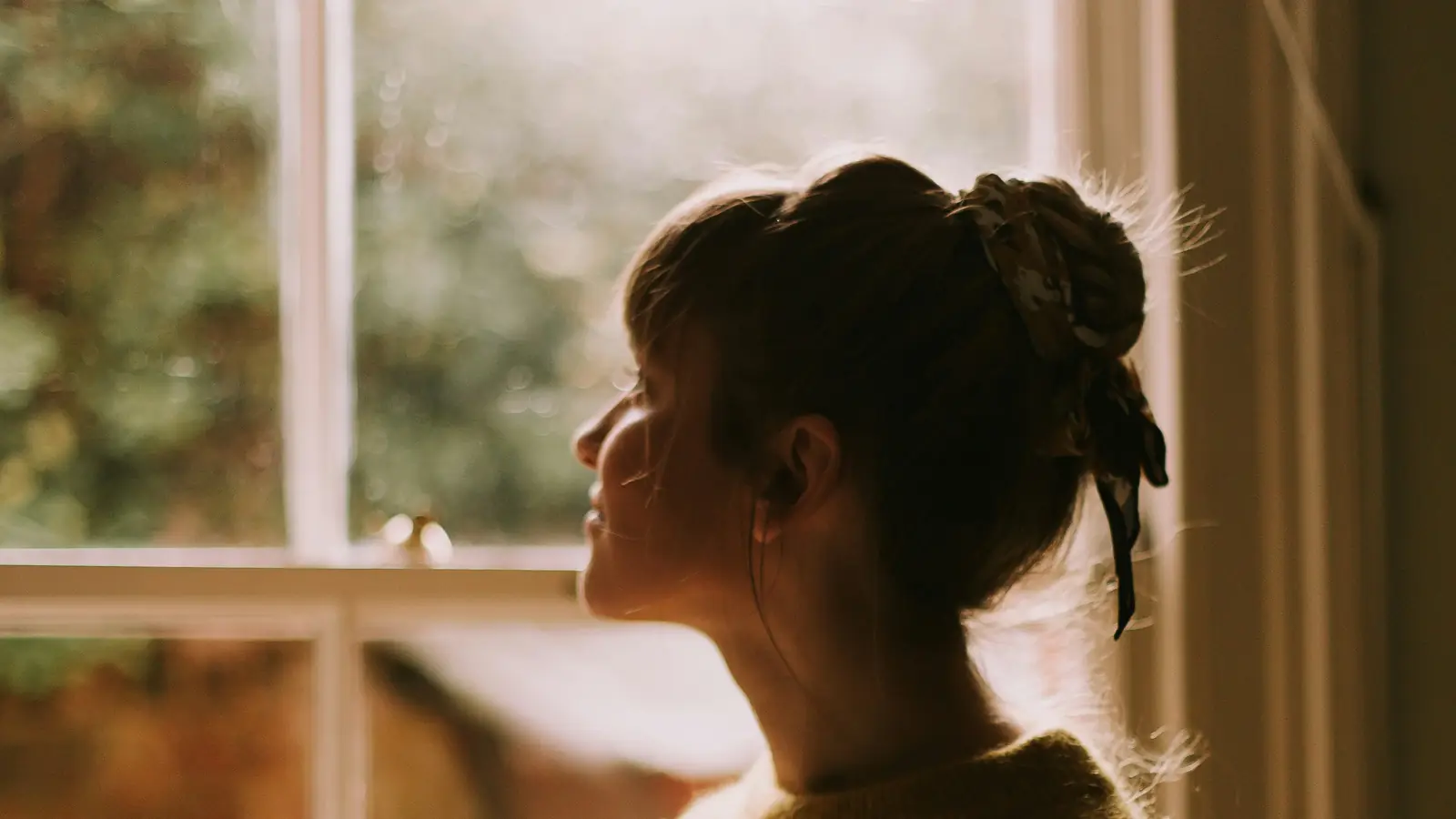 A woman gazing out a sunlit window